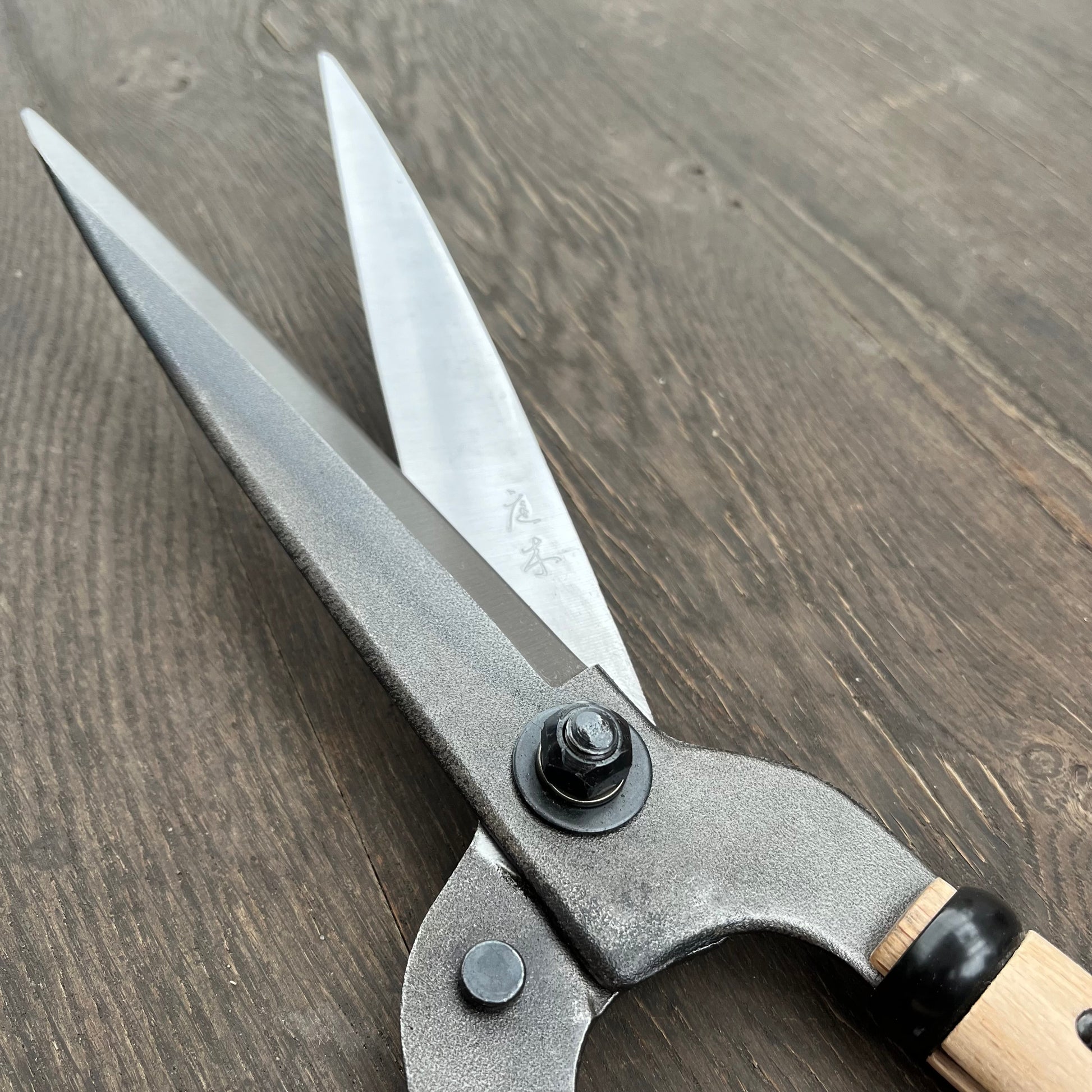 Eine Nahaufnahme der Niwaki FSC Heckenschere von Niwaki mit scharfen silbernen Klingen und einem Holzgriff aus FSC-zertifiziertem Holz, der auf einer dunklen Holzoberfläche ruht.