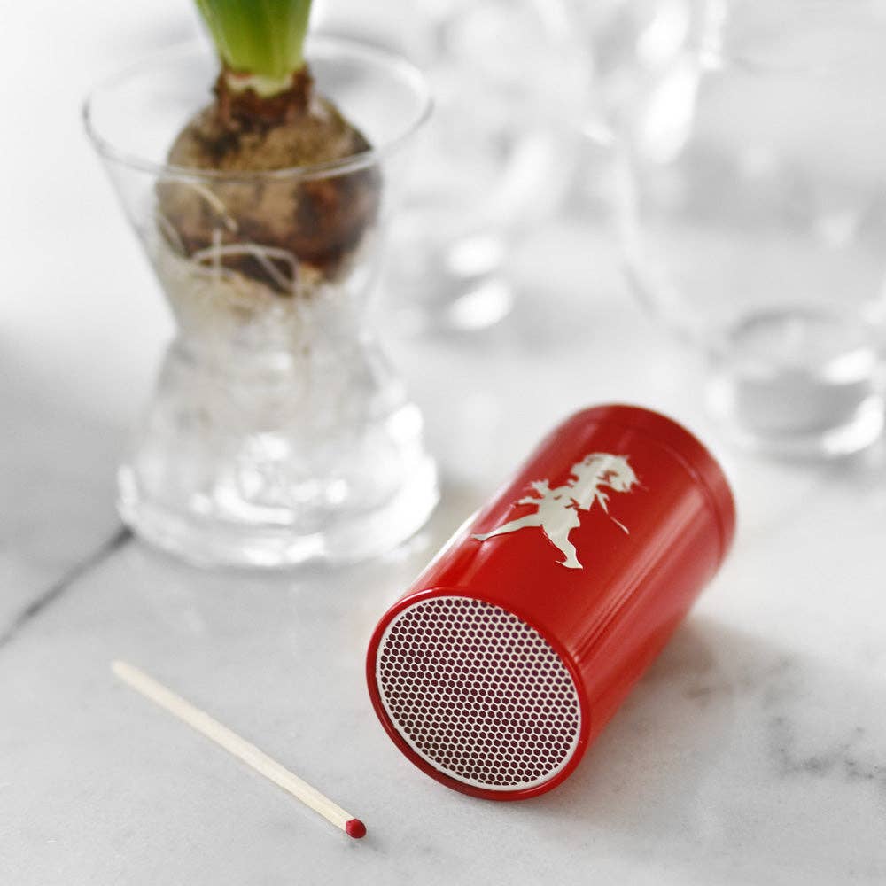 Ein roter Solstickan Design - Passender Schlauch (nur EU) liegt auf der Seite auf einer Marmorfläche neben extra langen Streichhölzern, mit einer Glasvase mit einer Zwiebelpflanze im Hintergrund.