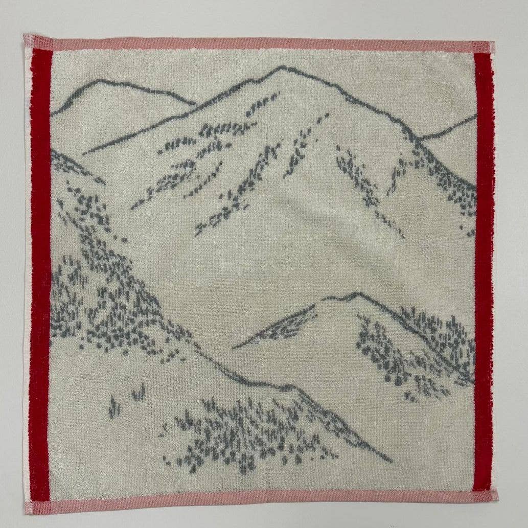 Das Küchenhandtuch "Grandeur nature" von Sylvie Thiriez ist ein weißes Baumwollhandtuch mit roter Bordüre und einem grauen, skizzenhaften Berg- und Baummotiv.
