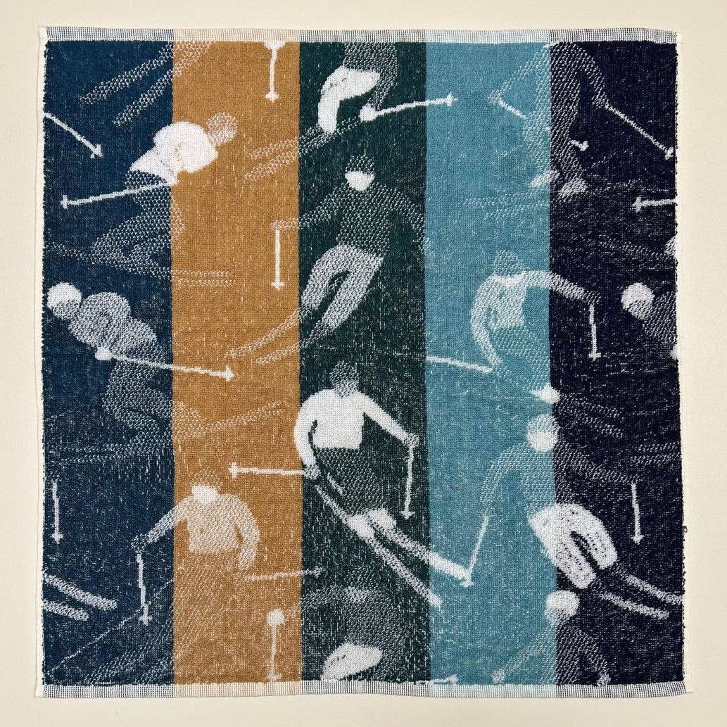 Das Küchenhandtuch "Skifahrer" von Sylvie Thiriez zeigt vertikale hellbraune, grüne, blaugrüne und marineblaue Streifen mit der Silhouette eines Skifahrers in Bewegung. Hergestellt in Portugal für dauerhafte Qualität.