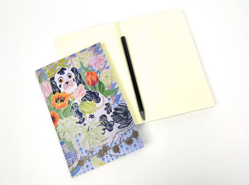 Das Art Angels - Wally Dogs and Tulpen Notizbuch von Angie Lewin, das einen Hund inmitten von Tulpen zeigt, ist auf einem aufgeschlagenen leeren Notizbuch mit einem schwarzen Stift auf der rechten Seite abgebildet, alles ordentlich auf einer weißen Fläche angeordnet.