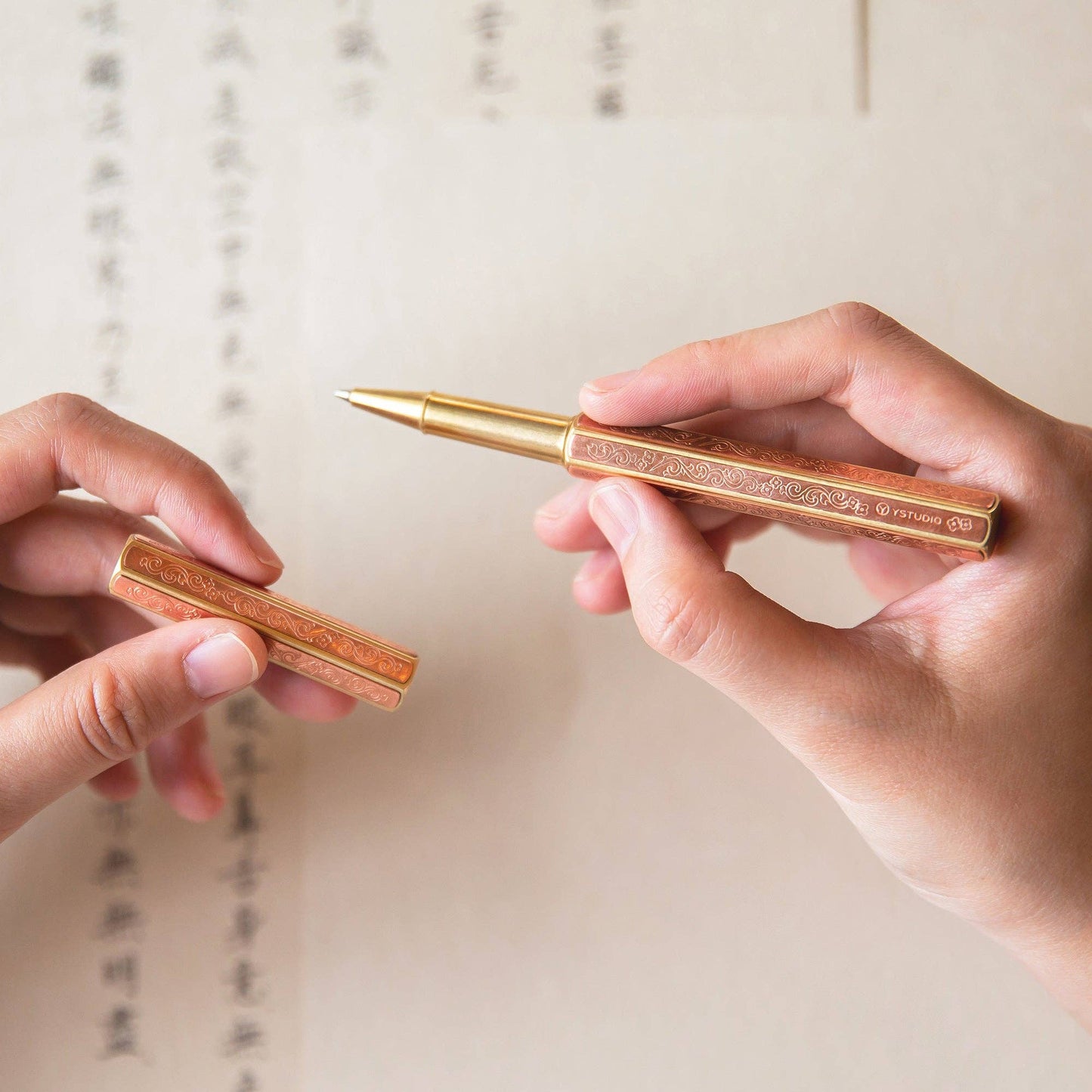 Eine Person hält den ENTREPÔT - YSTUDIO Klassische Renaissance KAZARI KANAGU ORCHID Tintenroller mit eingravierten, von Kazari Kanagu inspirierten Motiven über einem Blatt mit kursiver Schrift und asiatischen Zeichen.