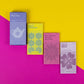 Vier Piccolo Seeds | Kollektion "Tees mit Blumen" Pakete von Piccolo Seeds mit den Bezeichnungen Floral Teas, Kamille Samen, Panorama Mix Monarda (Bee Balm) und Zebrina Mallow sind auf einem rosa-gelben Hintergrund angeordnet. Jede gentechnikfreie Packung zeigt eine einfache florale Illustration.