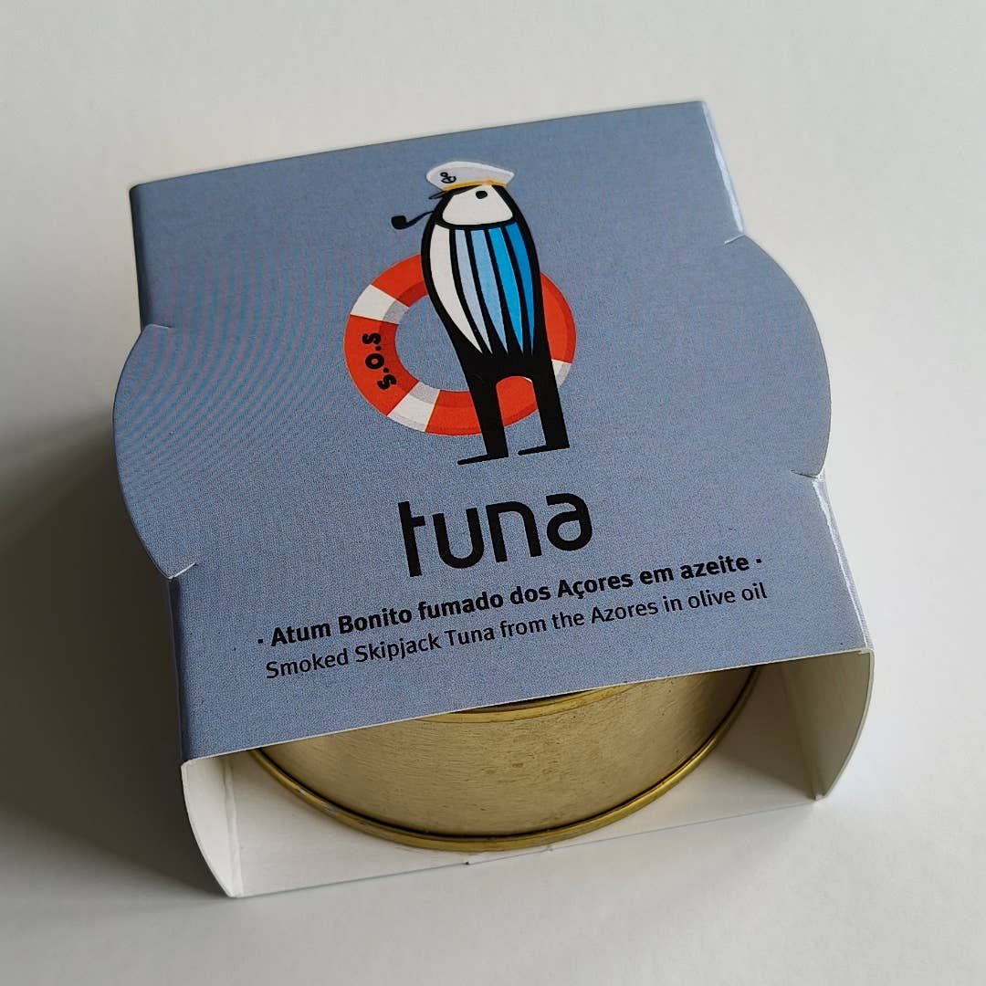 Eine Dose Sardinha - Geräucherter Bonito-Thunfisch aus den Azoren in Olivenöl, teilweise verpackt in einer hellblauen Schachtel mit einem Cartoon-Seevogel und zweisprachigem Text in Portugiesisch und Englisch.
