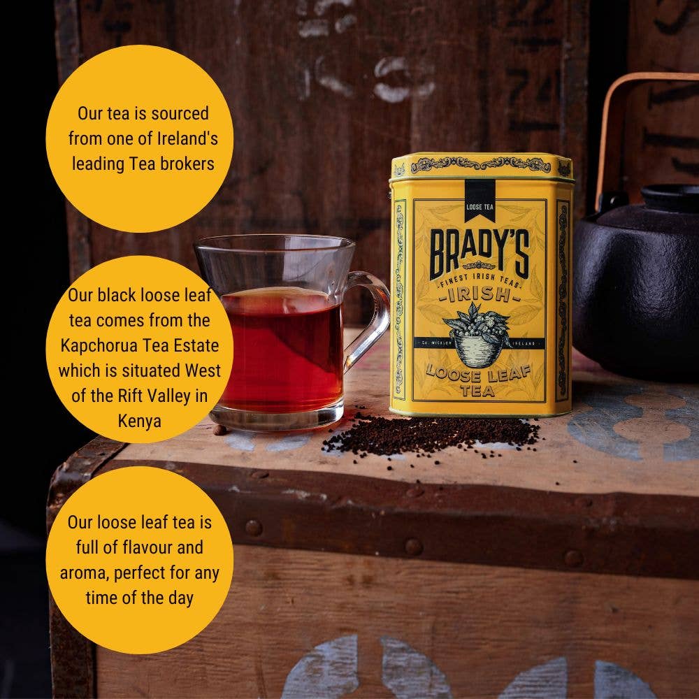 Eine Dose Brady's Coffee Company – Bradys Loose Leaf Tea und eine Glastasse stehen auf einer rustikalen Holzoberfläche mit verstreuten Teeblättern; Infoblasen heben das reiche Aroma des Tees hervor.