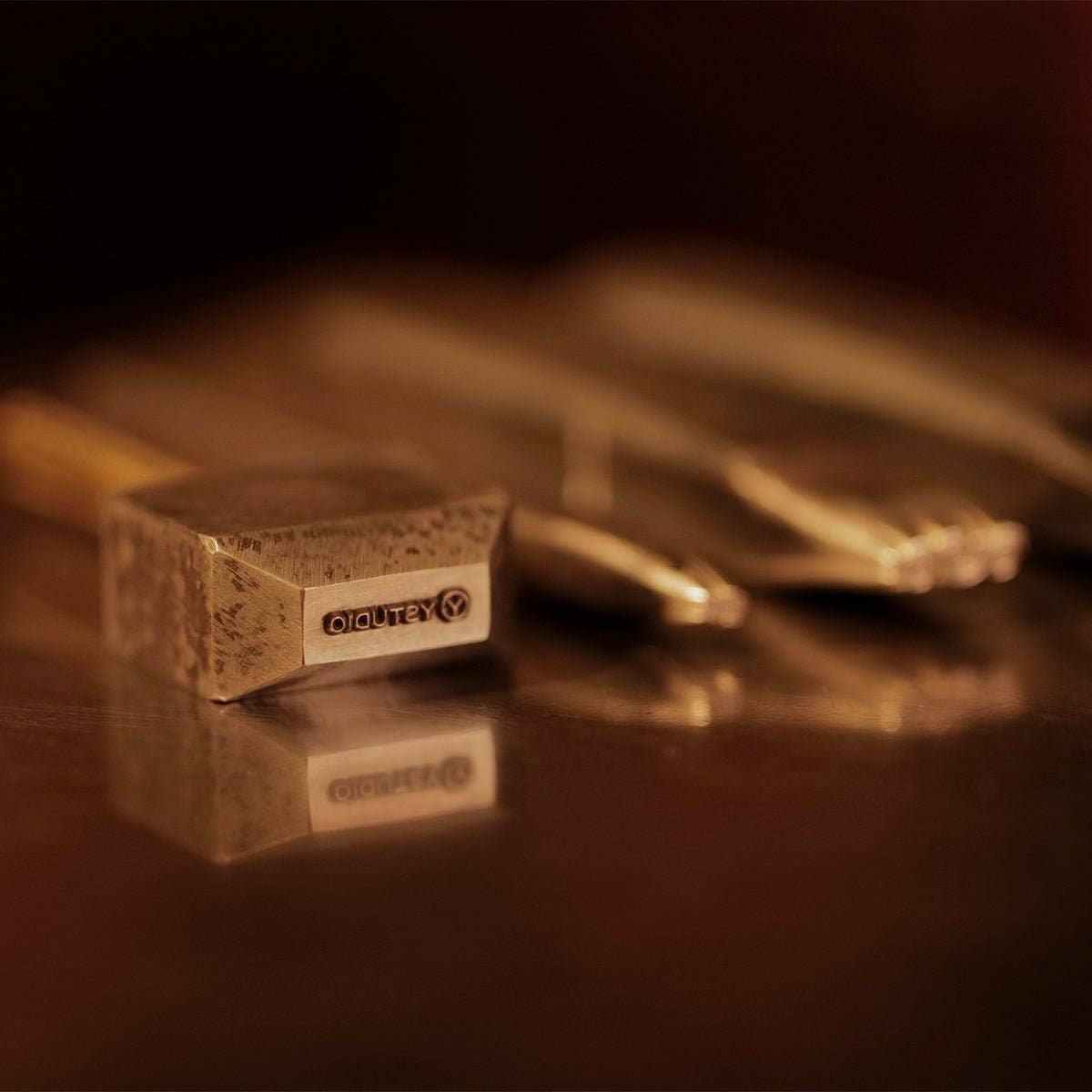 Eine Nahaufnahme des ENTREPÔT - YSTUDIO Klassische Renaissance KAZARI KANAGU ORCHID Tintenrollers mit feinen Gravurdetails, der auf einer spiegelnden Oberfläche inmitten von verschwommenen Metallwerkzeugen im Hintergrund ruht.