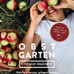 Eine Frau liegt lächelnd mit Äpfeln im Gras, umgeben von Körben. Das Buch „Obstgarten – einfach machen!“ aus dem Verlag Eugen Ulmer zeigt spielerisch gestaltete Anleitungen zum Obstanbau – ein frischer Ratgeber für den Garten.