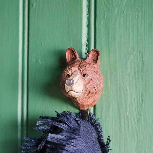 Ein handgeschnitzter Wandhaken aus Holz | Braunbär von Wildlife Garden hält einen dunkelblauen Stoff an einer grünen Holzvertäfelung - ein originelles Geschenk für Naturliebhaber.