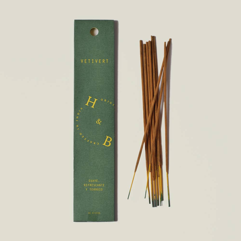Eine grüne Schachtel H&B Incense - De Vetivert Natürlicher Weihrauch mit der Aufschrift "Vetivert" und "Suave, refrescante y terroso" liegt neben einem Bündel brauner Räucherstäbchen auf hellem Grund, was auf seine beruhigende Wirkung schließen lässt.
