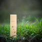 Eine beigefarbene rechteckige Schachtel mit der Aufschrift H&B Weihrauch - Natürlicher Vanille-Weihrauch steht aufrecht im grünen Gras und strahlt mit ihrem natürlichen Aussehen eine beruhigende Stimmung aus. Der weiche, verschwommene Hintergrund schafft eine friedliche Szene für Liebhaber von Vanille-Weihrauch.