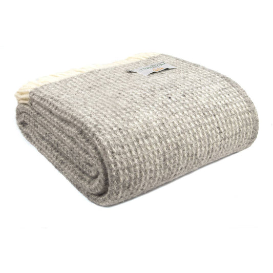 A folded grey Tweedmill | Waffeldecke Extra Groß Reine Neue Wolle aus reiner neuer Wolle mit Waffelstruktur und cremefarbenen Fransen. Das sichtbare Markenlabel von Tweedmill Textiles ist auf der Oberseite angebracht.