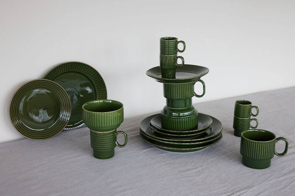 Ein dunkelgrünes Set der Sagaform GmbH Coffee & More Teetasse (2-tlg.) ist auf einer grauen Fläche arrangiert, wobei Tassen und Teller kreativ in der Mitte gestapelt und teilweise separat um sie herum platziert sind.