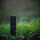 Eine schwarze, rechteckige Schachtel mit H&B Weihrauch - Natürlicher Oud-Weihrauch steht aufrecht in grünem Gras mit einem verschwommenen natürlichen Hintergrund, der an den holzigen Duft von natürlichem Oud und Weihrauch erinnert.