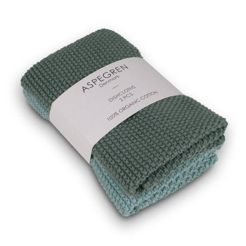 Zwei gefaltete, gestrickte Aspegren Denmark Spültücher in soliden Kieferntönen sind mit einem weißen Band mit der Aufschrift "Aspegren Denmark, Spültücher, gestrickt, massiv, Kiefernholz" zusammengebunden.