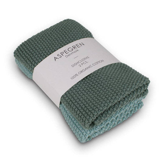 Zwei gefaltete, gestrickte Aspegren Denmark Spültücher in soliden Kieferntönen sind mit einem weißen Band mit der Aufschrift "Aspegren Denmark, Spültücher, gestrickt, massiv, Kiefernholz" zusammengebunden.