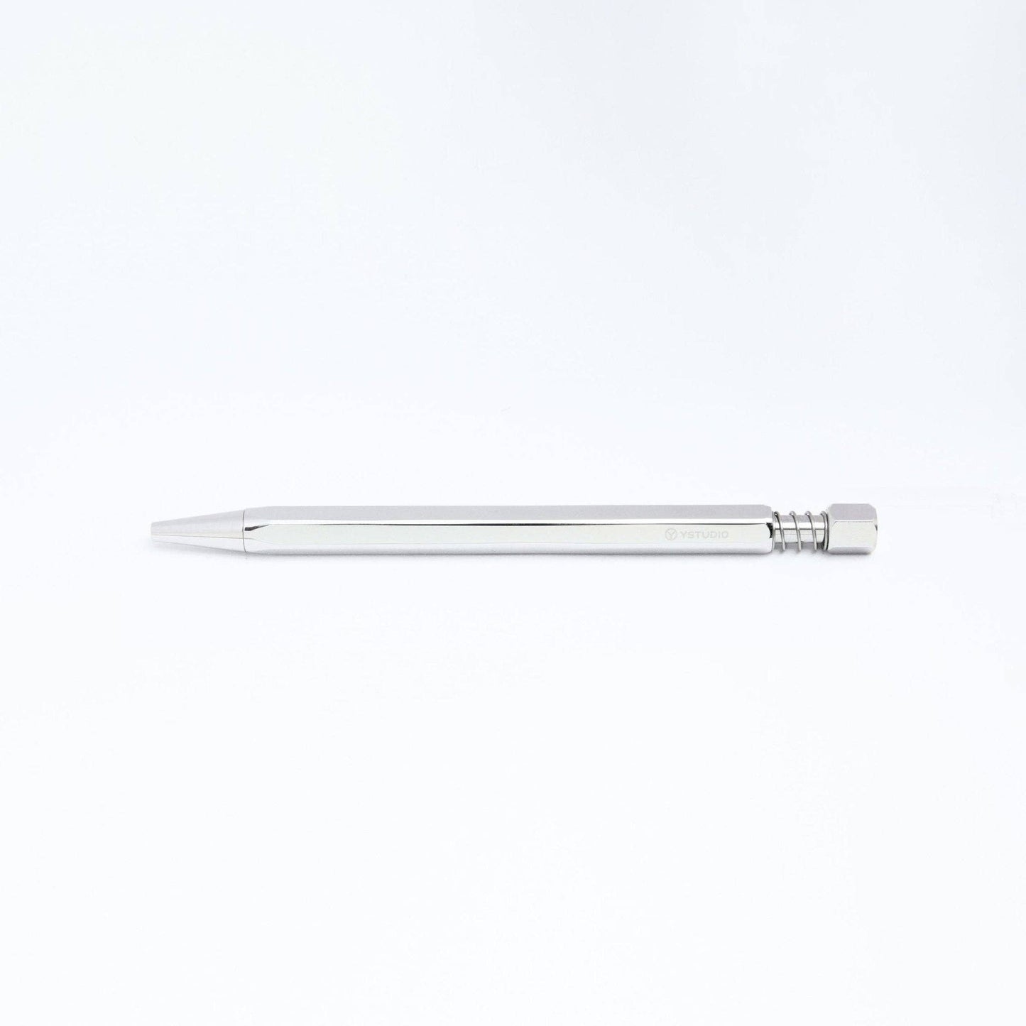 An ENTREPÔT YSTUDIO Klassischer Drehkugelschreiber Feder in glänzendem Silber mit metallischem, hexagonalem Gehäuse liegt waagerecht auf weißem Untergrund.