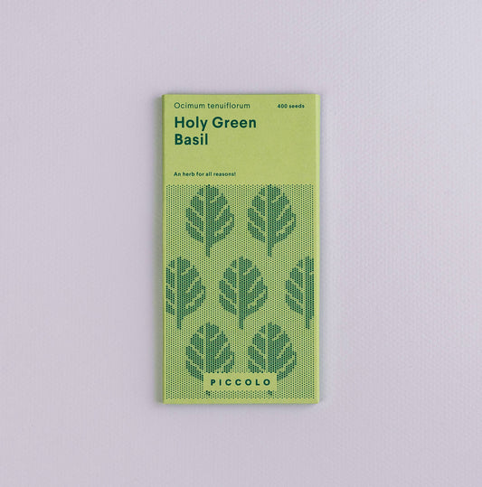 Eine grüne Packung Piccolo Seeds – Basil Heiliges Grün mit Blattillustrationen und 400 Samen trägt auf der Unterseite die Marke Piccolo Seeds. Sie liegt auf einer hellvioletten Oberfläche.