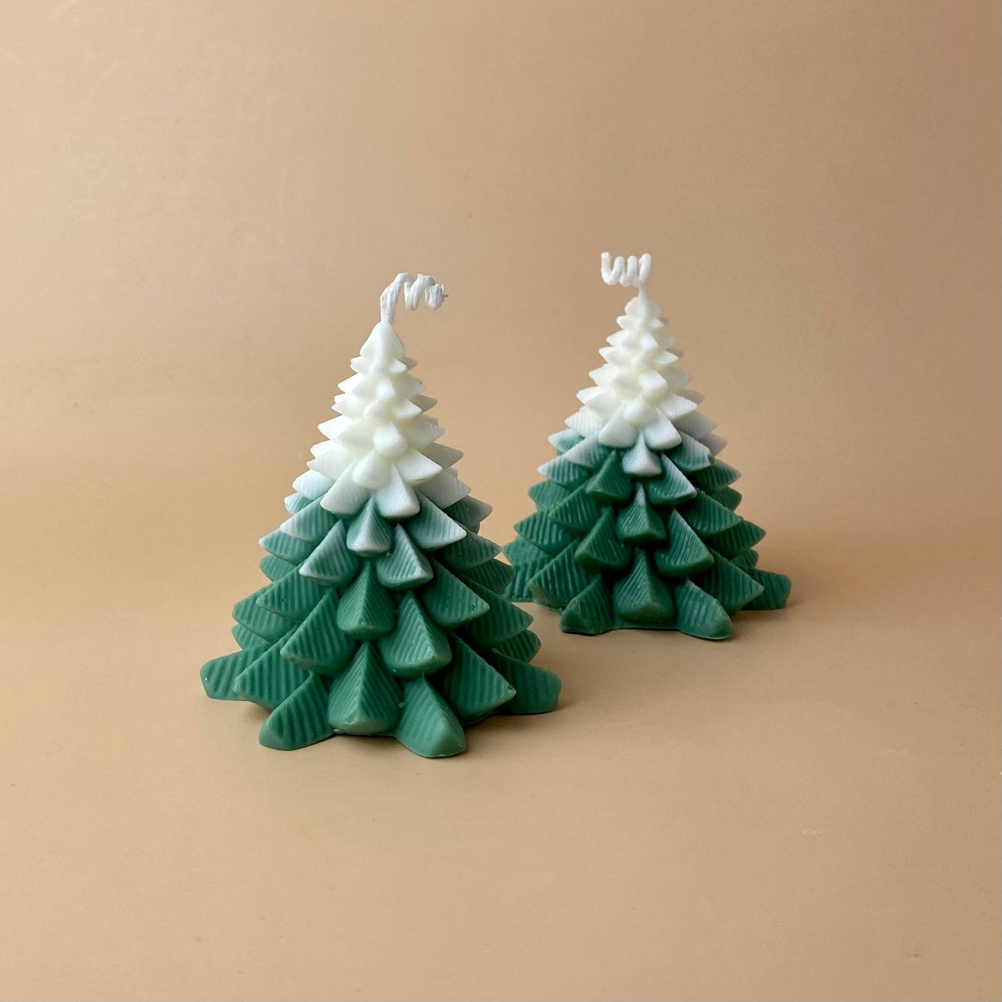 Zwei SOULCandle - Weihnachtskerzen von SOULCandle, grüne und weiße Kerzen in Tannenbaumform aus umweltfreundlichem Sojawachs, werden auf einem schlichten beigen Hintergrund präsentiert.