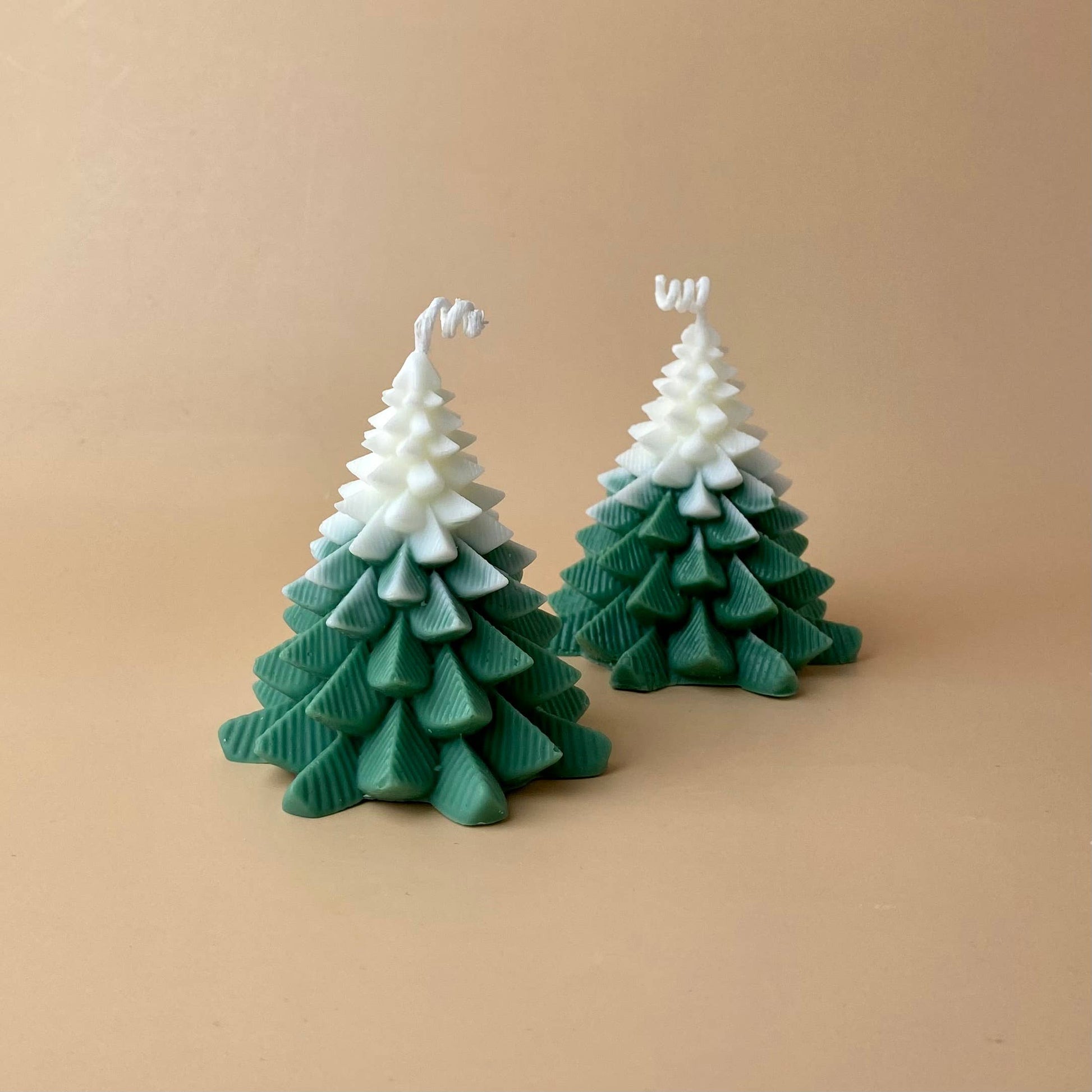 Zwei SOULCandle - Weihnachtskerzen von SOULCandle, grüne und weiße Kerzen in Tannenbaumform aus umweltfreundlichem Sojawachs, werden auf einem schlichten beigen Hintergrund präsentiert.