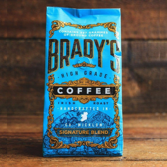 Eine blaue Tüte Brady's Coffee Company - Brady's Signature Blend Kaffee ist mit auffälligen goldenen und schwarzen Details versehen, die die hochwertige irische Röstung hervorheben, die von Brady's Coffee Company in der Grafschaft Wicklow vor einem hölzernen Hintergrund handgefertigt wird.