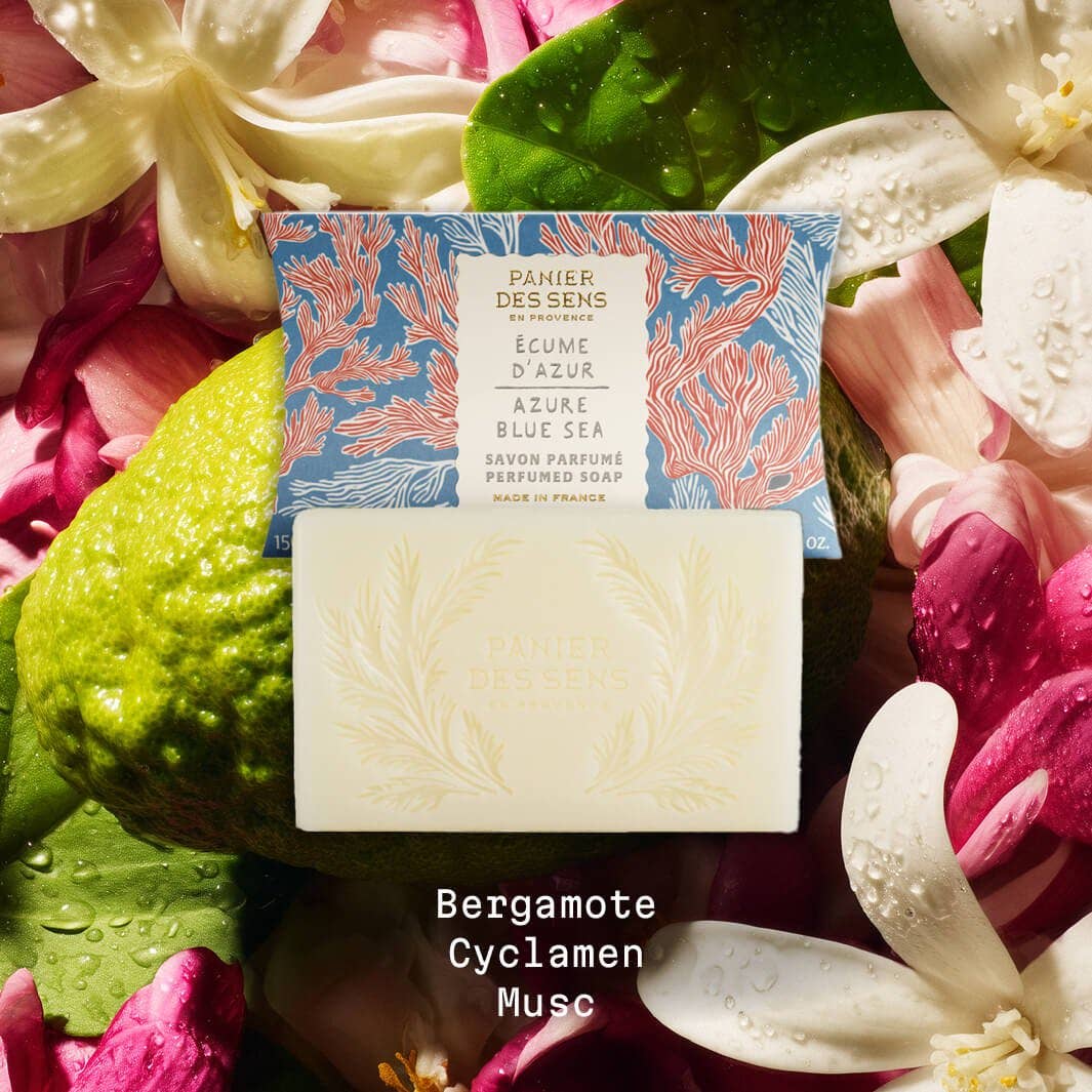 Ein Barren Panier Des Sens Duftseife | Ecume d'Azur 150 g liegt vor seiner dekorativen Schachtel, umgeben von weißen und rosa Blumen. Der Text darunter lautet: Bergamotte, Cyclamen, Musc.