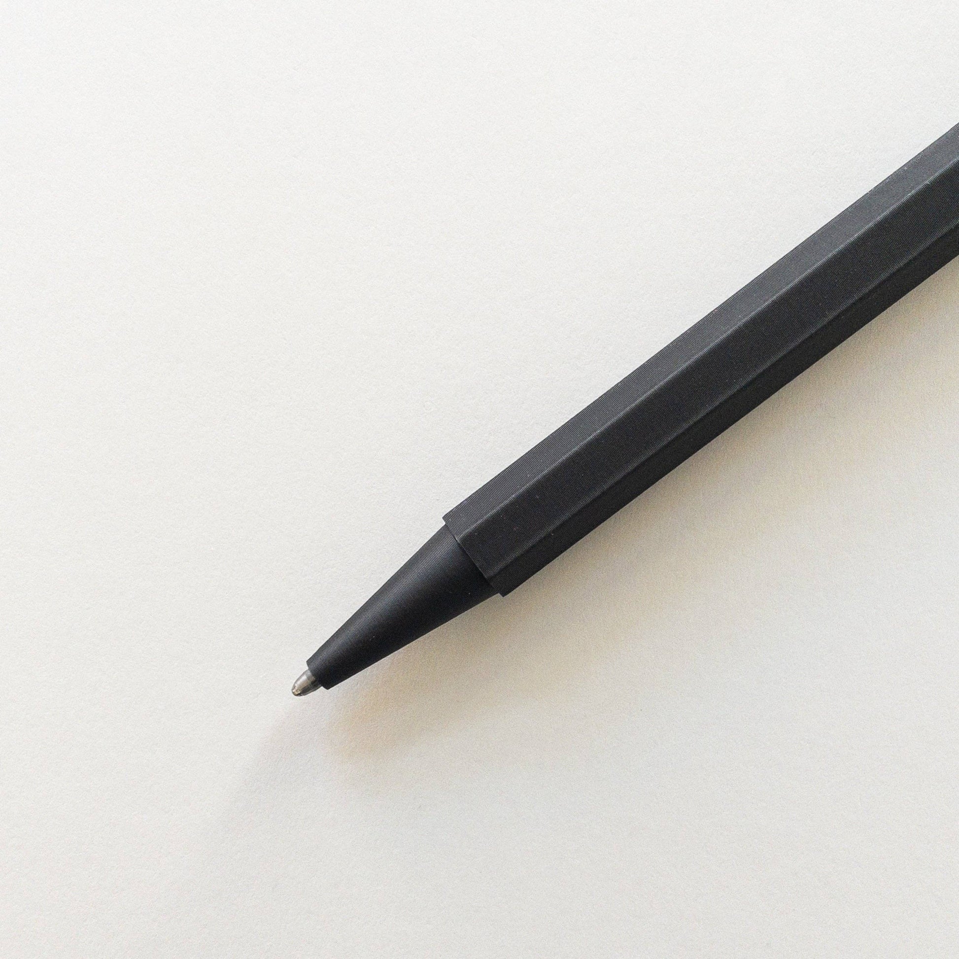 Der Prototo – Zero Waste Kugelschreiber in Schwarz von Prototo, ein klimaneutraler schwarzer Stift mit sechseckigem Schaft, liegt mit der Spitze auf die linke untere Ecke gerichtet auf einem leeren weißen Blatt Papier.