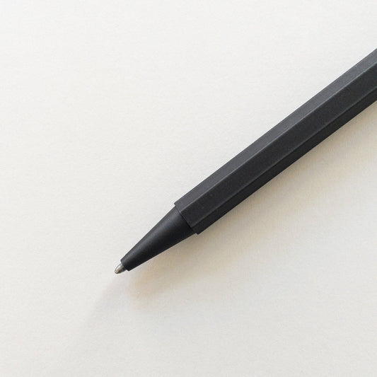 Der Prototo – Zero Waste Kugelschreiber in Schwarz von Prototo, ein klimaneutraler schwarzer Stift mit sechseckigem Schaft, liegt mit der Spitze auf die linke untere Ecke gerichtet auf einem leeren weißen Blatt Papier.