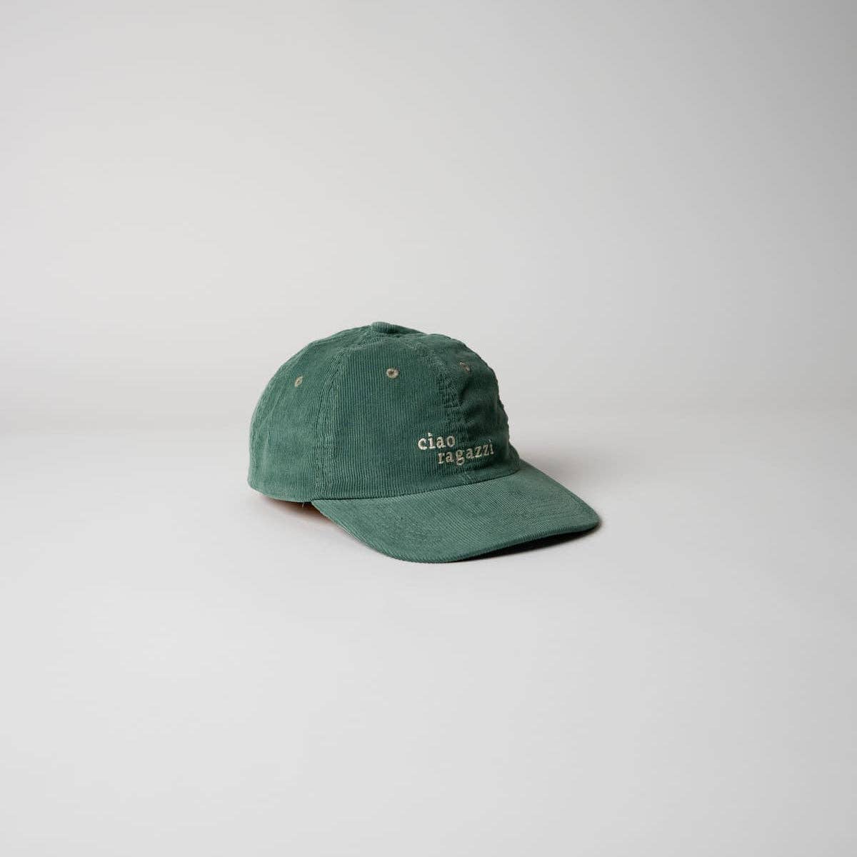 Die grüne "Ciao ragazzi" Premium Cord Dad Cap von arrel - responsible apparel aus Bio-Baumwolle zeigt den weißen Schriftzug auf der Vorderseite und wird auf hellem, schlichtem Hintergrund präsentiert.
