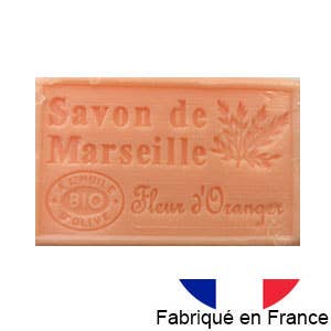 Eine rechteckige orangefarbene Tafel von Dampa 1975 Marseiller Seife mit Bio-Olivenöl-Orangenduft mit französischer Prägung, abgebildet neben einer kleinen französischen Flagge und der Aufschrift "Fabriqué en France".