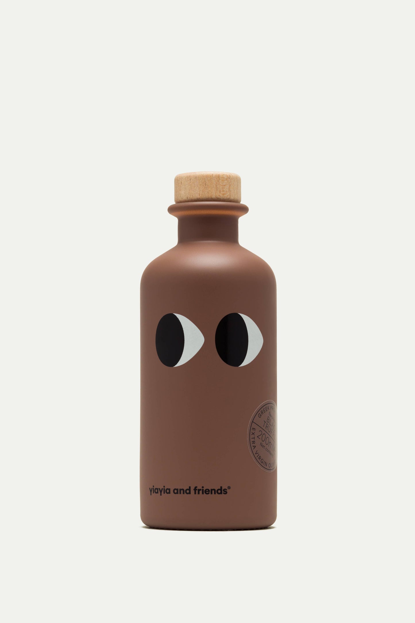 Eine braune Flasche mit einem Holzdeckel, zwei stilisierten Augen und dem Text "yiayia and friends" in der Nähe des Bodens enthält yiayia and friends - Natives Olivenöl extra mit Trüffel.