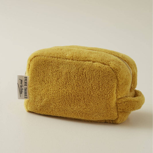 Die Sylvie Thiriez | Kulturbeutel Honigfarben aus Plüsch ist eine kleine, rechteckige Tasche mit oberem Reißverschluss, seitlichem Henkel und weißem SIXTY THREE 12-Tag auf heller, neutraler Oberfläche.