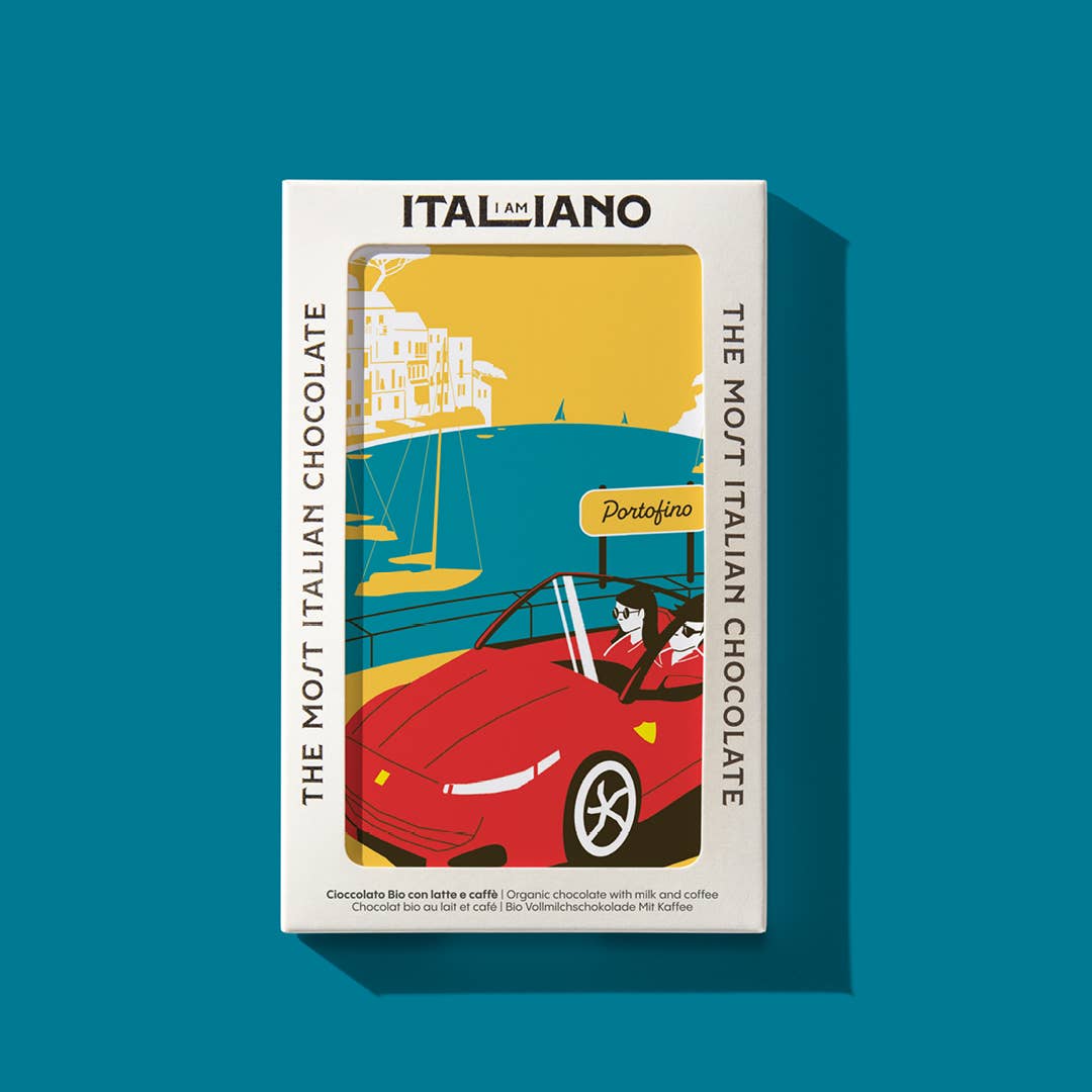 Eine Verpackung von I AM ITALIANO - Porto Fino Bio-Schokolade mit Milch und Kaffee zeigt eine Frau in einem roten Cabrio am Meer in Portofino, Italien. Der Text lautet ITALIANO und The Most Italian Chocolate-perfekt mit Ihrem Lieblingskaffee.