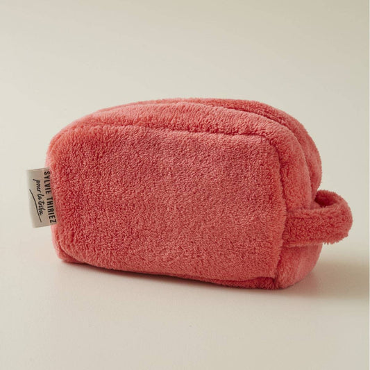 Ein kleiner, rechteckiger Sylvie Thiriez | Kulturbeutel Flamingofarben aus Plüsch in zartem Rosa, mit kurzem Henkel und Seitenetikett, wird auf eine helle Fläche gestellt.