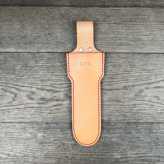 Ein hellbraunes Niwaki Long Holster von Niwaki mit roten Nähten und japanischer Prägung im oberen Bereich liegt flach auf einer Holzoberfläche. Es wurde für große Scheren entworfen und verfügt über eine Gürtelschlaufe zur einfachen Befestigung.
