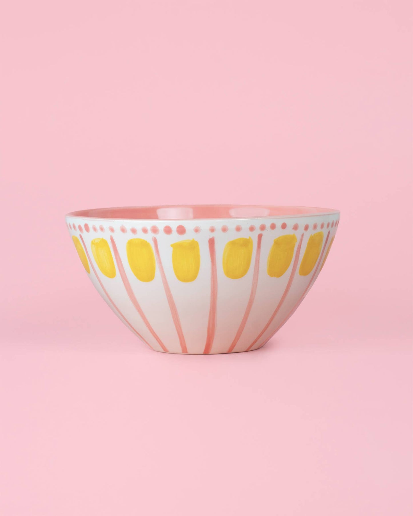 Die Alfar Tierra Cocida VALENTINA 1,5L handgefertigte Keramik-Servierschale in Rosa und Gelb besitzt eine weiße Basis mit pinken Streifen und gelben Ovalen, abgebildet vor einem rosa Hintergrund.