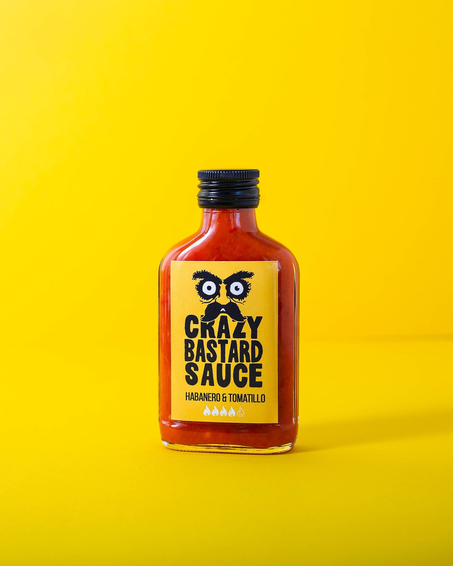 Eine 100-ml-Flasche CBS Foods GmbH (Crazy Bastard Sauce) - Habanero & Tomatillo scharfe Soße hat ein gelbes Etikett mit schwarzer Schrift und illustrierten Augen vor leuchtend gelbem Hintergrund.