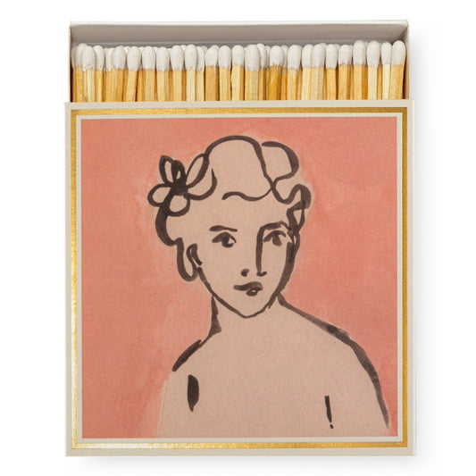 Die Archivist Gallery - Divine | Square - Sicherheitsspiele ist eine Streichholzschachtel mit einem rosafarbenen Umschlag, auf dem eine schwarze Strichzeichnung einer Frau mit stilisiertem Haar und einer Blume in Gold abgebildet ist - ein elegantes Geschenk der Archivist Gallery.