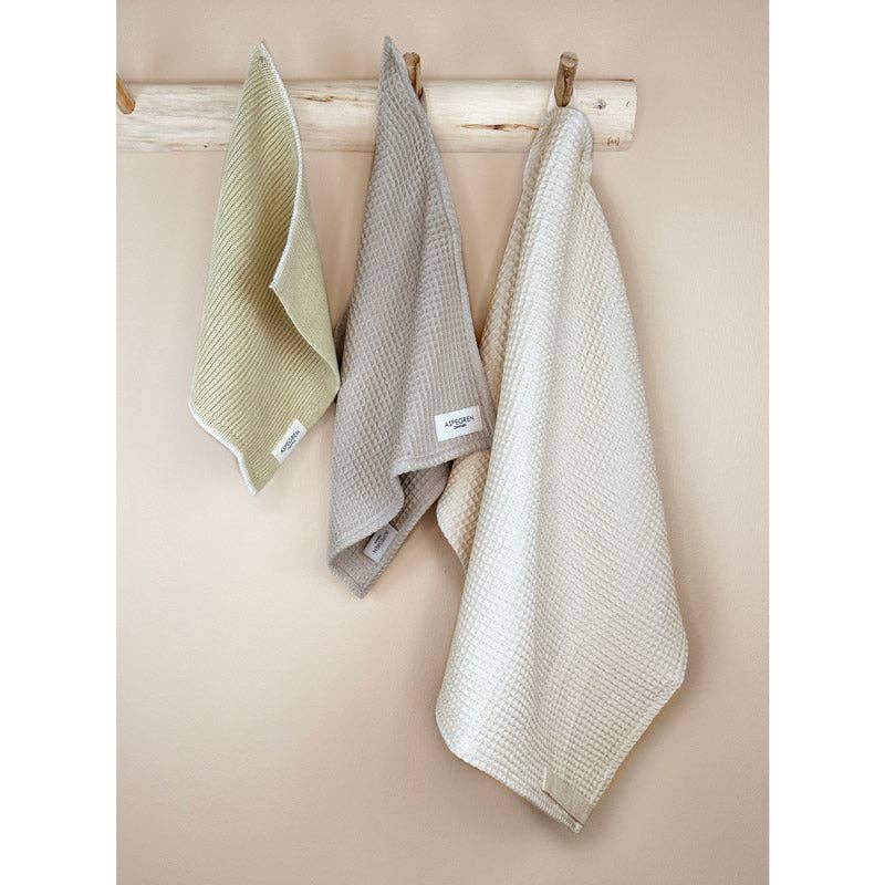 Drei strukturierte Handtücher von Aspegren Denmark aus dem Geschenkset Lemon Grass (Hellgrün, Beige, Cremeweiß) hängen an einem Holzständer – ein umweltfreundliches Geschenkset, perfekt für jede Küche.