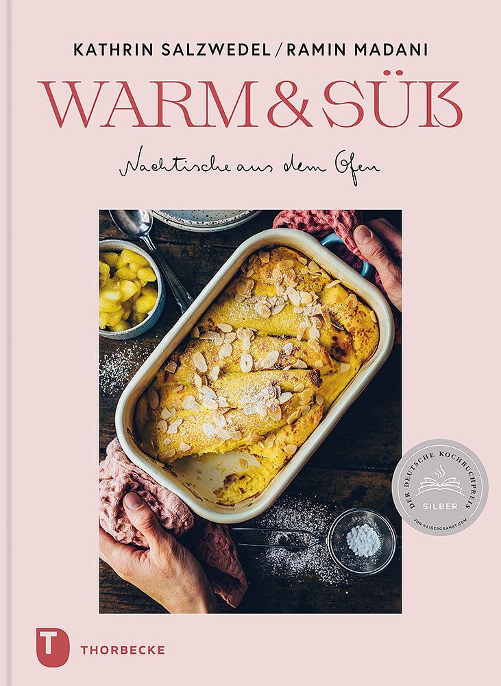 Das Cover von „Warm & Süß“ aus dem Thorbecke Verlag zeigt ein gebackenes Dessert mit gesplitterten Mandeln in einer weißen Schale, umgeben von Händen, Früchten und einem Sieb.