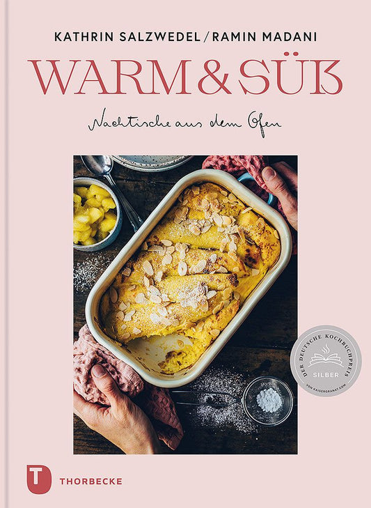 Das Cover von „Warm & Süß“ aus dem Thorbecke Verlag zeigt ein gebackenes Dessert mit gesplitterten Mandeln in einer weißen Schale, umgeben von Händen, Früchten und einem Sieb.
