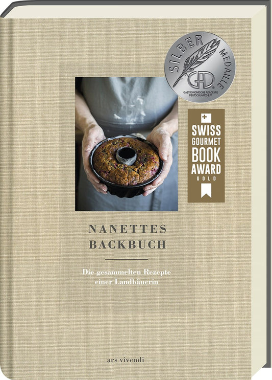 Das Cover von Nanettes Backbuch aus dem Ars Vivendi Verlag zeigt Hände, die einen Marmorkuchen in einer Pfanne halten, auf einem beigefarbenen, strukturierten Hintergrund, mit dem Siegel des Swiss Gourmet Book Award und der Silbermedaille oben rechts.