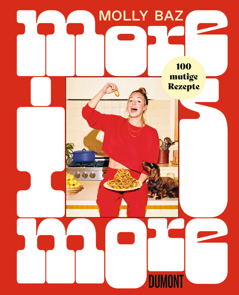 Eine Frau in Rot steht in einer Küche mit Essen, während ihr Hund aufschaut. Der Text ist fett gedruckt: More is More von Dumont Verlag - ein Kochbuch mit 100 kreativen, mutigen Rezepten.