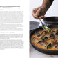 Eine Hand garniert gebackene gefüllte Auberginenröllchen in Curry-Kokos-Dal, inspiriert von Yotam Ottolenghis "Flavour" aus dem DK Verlag, mit geschnittenem Chili und Kräutern, mit kreativen veganen Rezepten und den Zutaten auf der linken Seite.