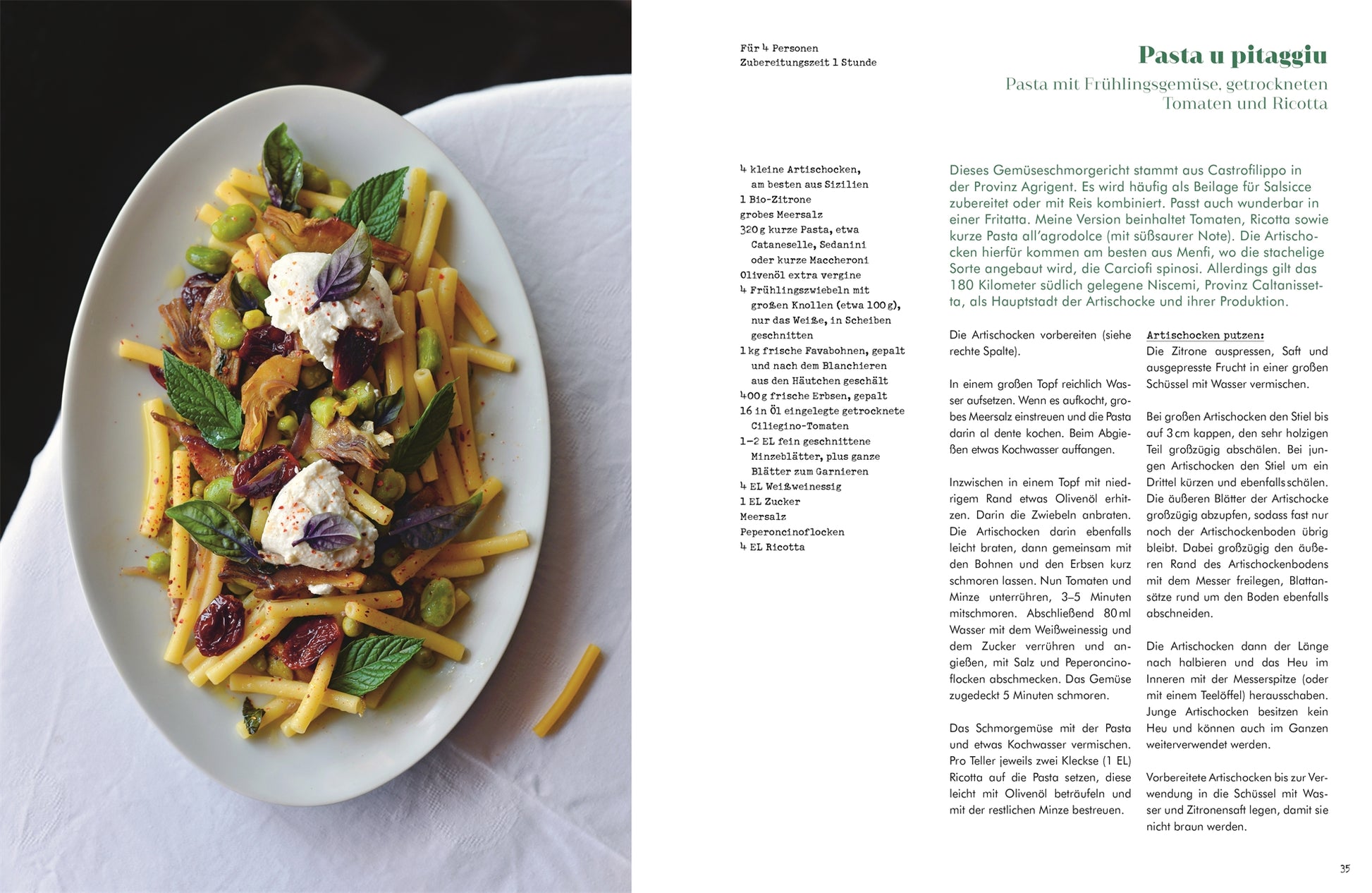 Auf einem dunklen Tisch steht ein weißer ovaler Teller mit gelben Nudeln, sonnengetrockneten Tomaten, Ricotta, Pistazien und Minze; auf der Seite daneben ist ein authentisches sizilianisches Rezept aus "Sizilien in meiner Küche" vom DK Verlag auf Deutsch abgebildet.