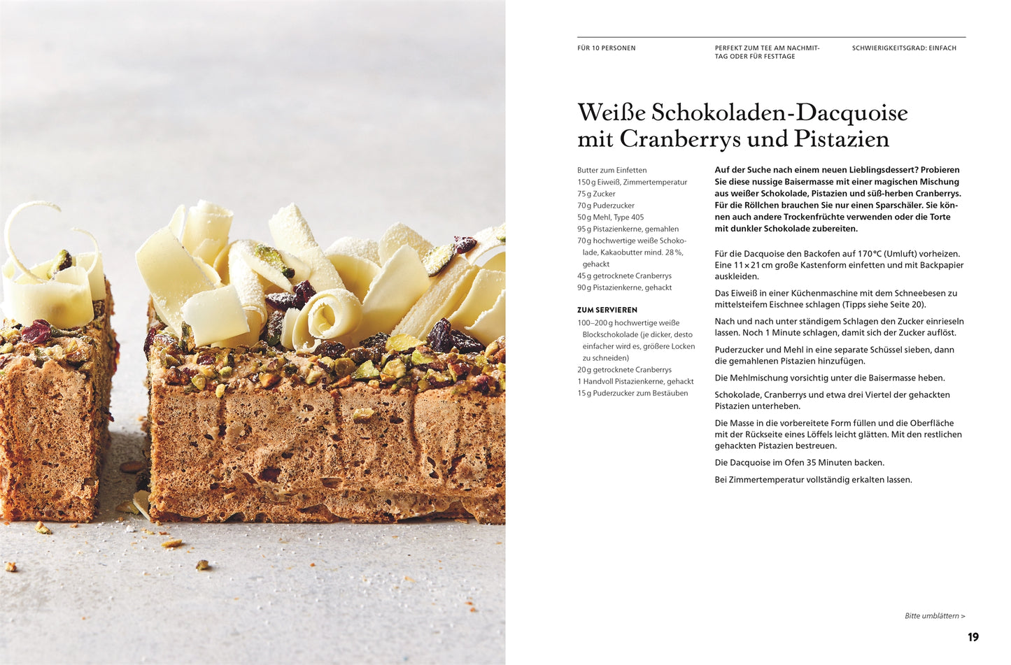 Ein rechteckiger Schokoladenkuchen, verziert mit weißen Schokoladenlocken, Pistazien und Cranberries auf grauem Untergrund, inspiriert von „Alles aus Schokolade“ vom DK Verlag – ein verführerischer Leckerbissen in Nahaufnahme mit minimalistischem Hintergrund.