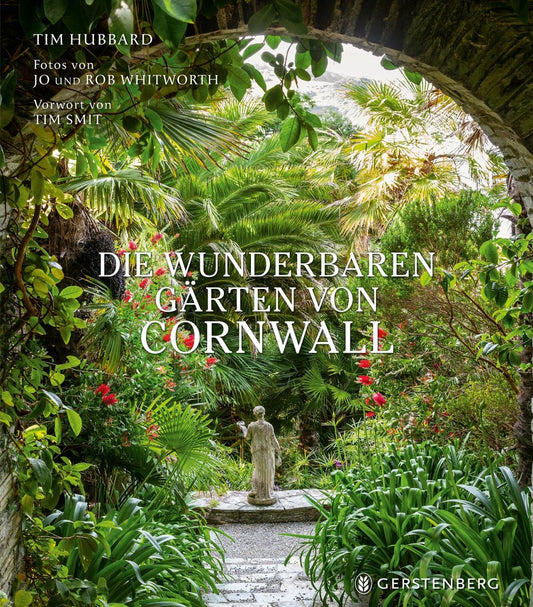 Das Titelbild von Die wunderbaren Gärten von Cornwall (Gerstenberg Verlag) zeigt einen üppigen Garten mit Palmen, roten Blumen und einer Steinstatue, die von einem alten Torbogen eingerahmt wird - eine Einladung, die schönsten englischen Gärten Cornwalls zu entdecken.