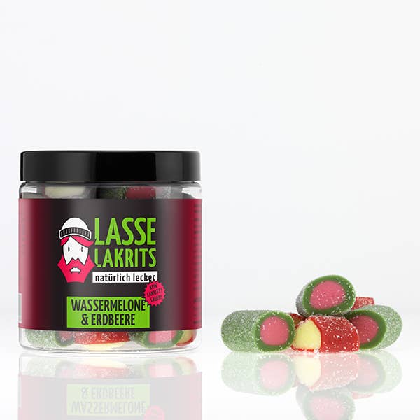 Eine LASSE LAKRITS Dose Saure Wassermelone & Saure Erdbeere mit dunklem Deckel und Cartoon-Gesicht sitzt auf einer weißen Fläche neben bunten, gezuckerten Fruchtgummi, und ist ohne Palmöl.