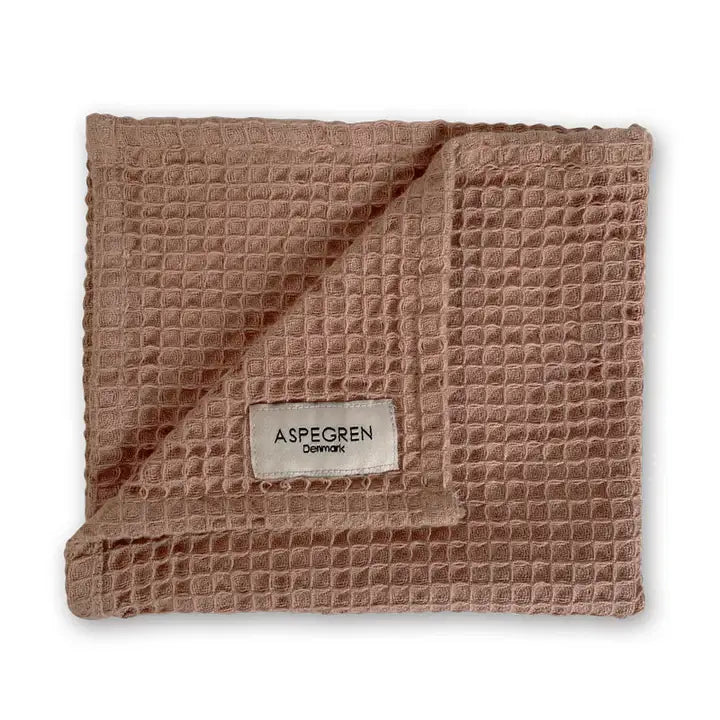 Ein gefaltetes hellbraunes Tuch mit Waffelstruktur, bei dem eine Ecke umgeschlagen ist und das ein weißes Etikett mit der Aufschrift Aspegren Denmark - ein nachhaltiges Geschirrtuch aus dem Geschenkset Praliné, ideal für die Küche - trägt.