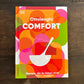 Das Bild zeigt das Cover von DKs Kochbuch – Ottolenghi „Comfort“ mit kräftigen, bunten überlappenden Kreisen, einer weißen Schöpfkellenillustration und dem deutschen Untertitel: Rezepte, die du lieben wirst – ideale Gerichte mit natürlichen Zutaten.