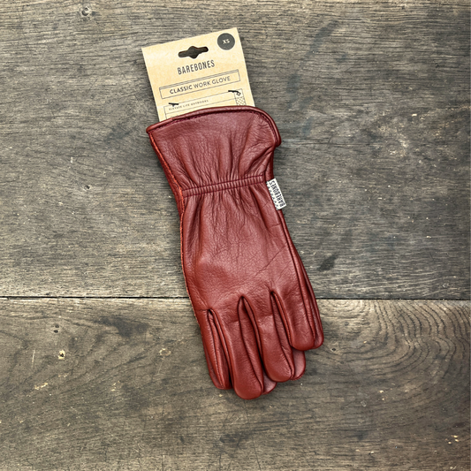 Ein einzelner Barebones Classic Gartenhandschuh aus Büffelleder 'Cognac' von Königliche Gartenakademie liegt auf Holz und trägt ein Etikett mit der Aufschrift "Classic Work Glove".